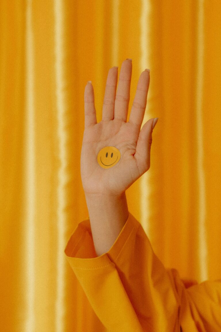 Una mano abierta contra una cortina amarilla, con una carita sonriente en la palma.