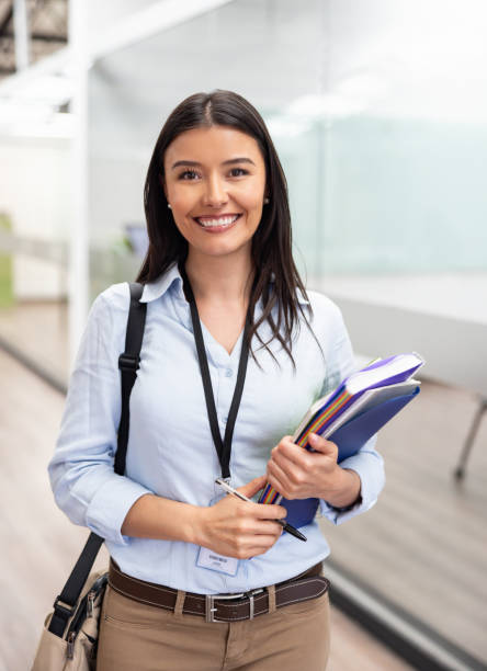 Profesora sonriendo con carpetas y apuntes en mano.